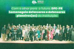 Imagem que mostra todos os defensores e defensoras presentes na cerimônia no palco do auditório. Acima da imagem está escrito o título da matéria.