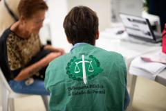 Servidor da Defensoria Pública usando coleta com a logo da instituição realiza atendimento de senhora idosa durante mutirão de atendimento. 