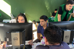 Imagem mostra três servidores utilizando computadores durante os atendimentos do mutirão. De costas em primeiro plano se vê um assistido.