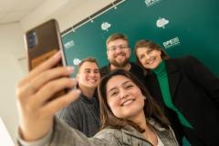 Servidor empossado hoje posa para selfie com a família em frente a backdrop da Defensoria. 