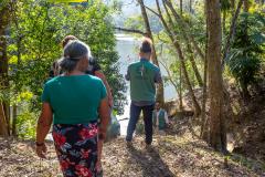 Imagem mostra mulher quilombola e um servidor da DPE-PR, ambos de costas, seguindo por trilha no quilombo. 