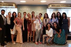 Vemos todos os participantes do evento em pé, juntos,  esperando a foto ser tirada. 