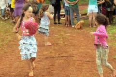 Crianças brincando, enquanto os moradores estão reunidos ao fundo.  