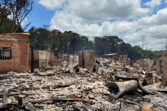 Foto mais ampla mostrando o que restou das estruturas pós incidente. Vemos muitos escombros e algumas paredes de tijolos ainda de pé.  
