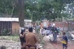 Imagem da reintegração de posse. Policiais no canto esquerdo da foto, no direito estão as pessoas desabrigadas carregando suas coisas.