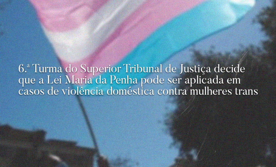 Na imagem, uma bandeira do movimento trans e uma manchate onde se lê: 6.ª Turma do Superior Tribunal de Justiça decide que Lei Maria da Penha pode ser aplicada em casos de violência doméstica contra mulheres trans