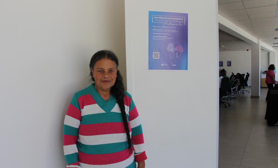 Imagem de usuária ao lado de cartaz de divulgação do mutirão