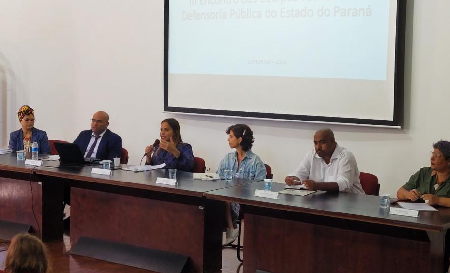 Imagem que mostra a mesa de abertura do evento, com a presença de seis pessoas, dois homens e quatro mulheres, que são representantes da Defensoria Pública e convidadas.