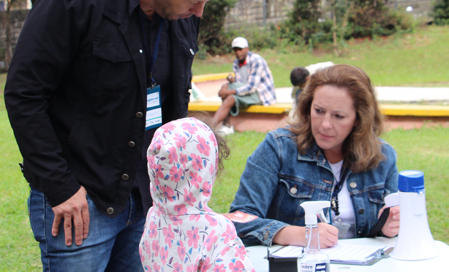 Imagem de uma servidora pública prestando orientação a um homem com sua filha.