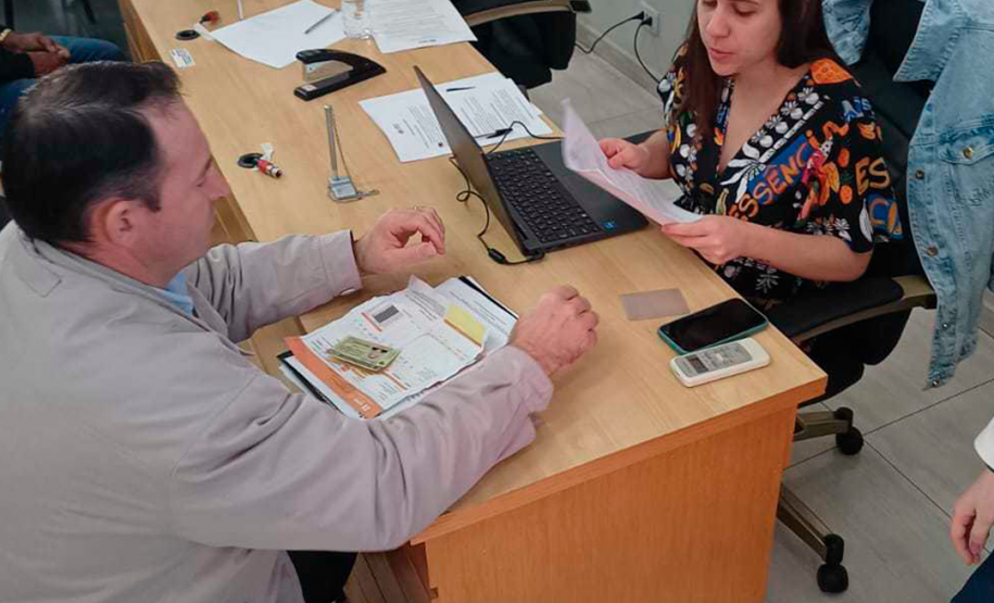 Imagem que mostra duas atendentes da Defensoria Pública. Uma delas está atendendo um homem que está com vários documentos a sua frente.