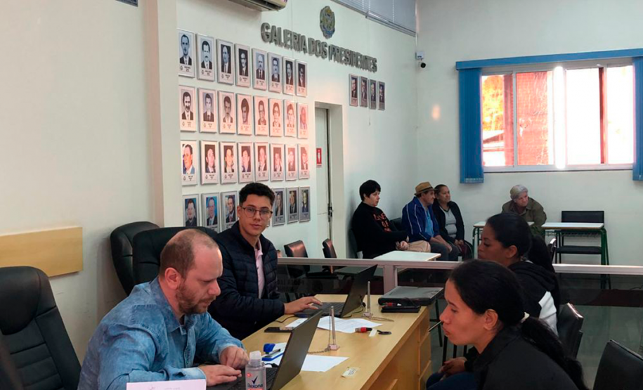 Imagem que mostra dois atendentes da Defensoria Pública, cada um deles está atendendo uma mulher. Ao fundo, pessoas aguardam atendimento.