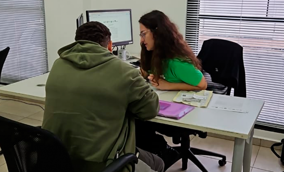 Imagem que mostra um atendimento no mutirão. Duas pessoas, cada uma de um lado, olham algo que está em cima de uma mesa.