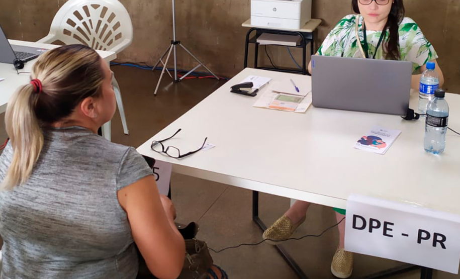 Imagem que mostra um atendimento no mutirão. Uma mulher atende outra mulher. Elas estão em uma mesa branca. A atendente usa um notebook.