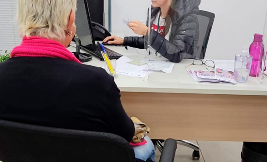 Imagem que mostra um atendimento do mutirão. A atendente da Defensoria analisa um papel e, em cima da mesa onde ela trabalha, estão cartilhas com o tema do mutirão.