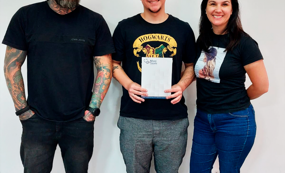 Imagem que mostra a usuária da DPE-PR Marty Cristine Maceno com seu filho e o pai dele, Clayton Teles dos Santos. Os três estão em pé, o filho ao centro, segurando uma pasta com o resultado do DNA.