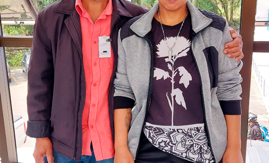 Imagem que mostra a usuária da DPE-PR Priscila Patrícia Rodrigues ao lado do pai. Eles estão de pé e o pai está com uma das mãos no ombro da filha.