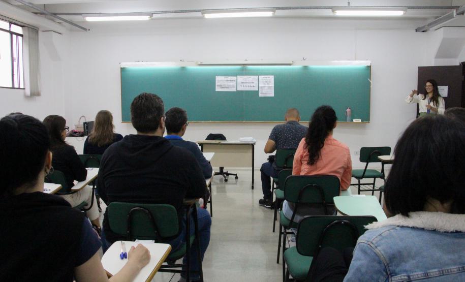Imagem que mostra uma das salas de aplicação de prova do concurso. Candidatos e candidatas estão de costas, sentados em carteiras de frente para um quadro onde estão coladas folhas com as instruções da prova.