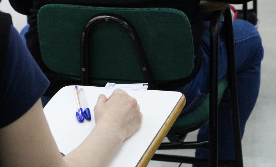 Imagem que foca no braço de uma candidata, que está pousado sobre uma carteira, ao lado de duas canetas.