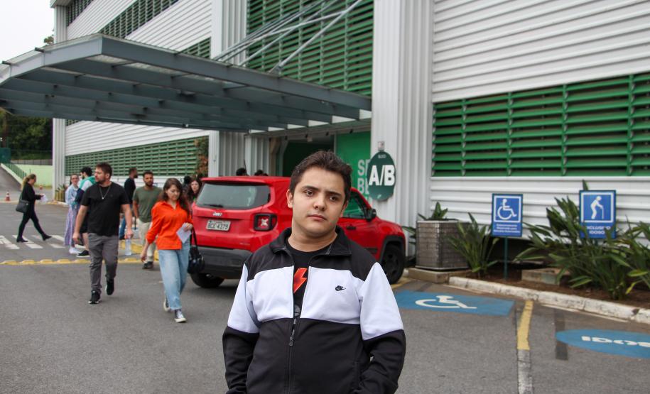 Imagem que mostra o candidato Daniel Victor Machado Raymundo em frente ao local de prova, um dos prédios da Universidade Tuiuti, em Curitiba. Ele veste uma blusa esportiva nas cores preta e branca.