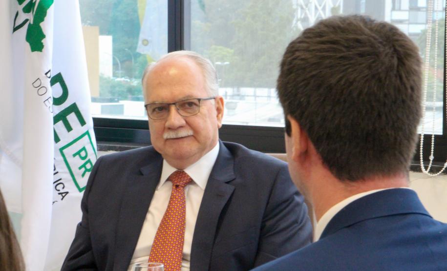 Imagem do Ministro Fachin sentado à mesa e olhando para o defensor público Matheus Munhoz, com quem estáva conversando no momento.