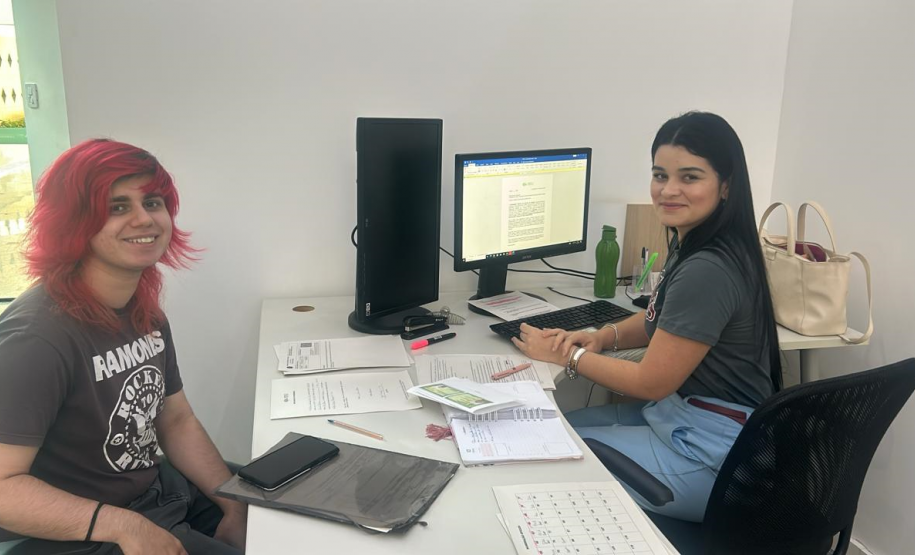 Imagem de uma foto em um ângulo aberto de um atendimento, o servidor público e o usuário posam sorrindo para a foto.