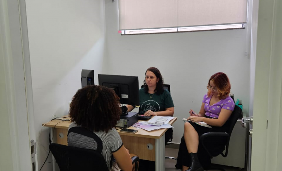 Imagem de um atendimento ocorrendo em uma sala branca, na foto, uma servidora pública usando a camiseta da Defensória Pública do Estado do Paraná está fazendo o atendimento.