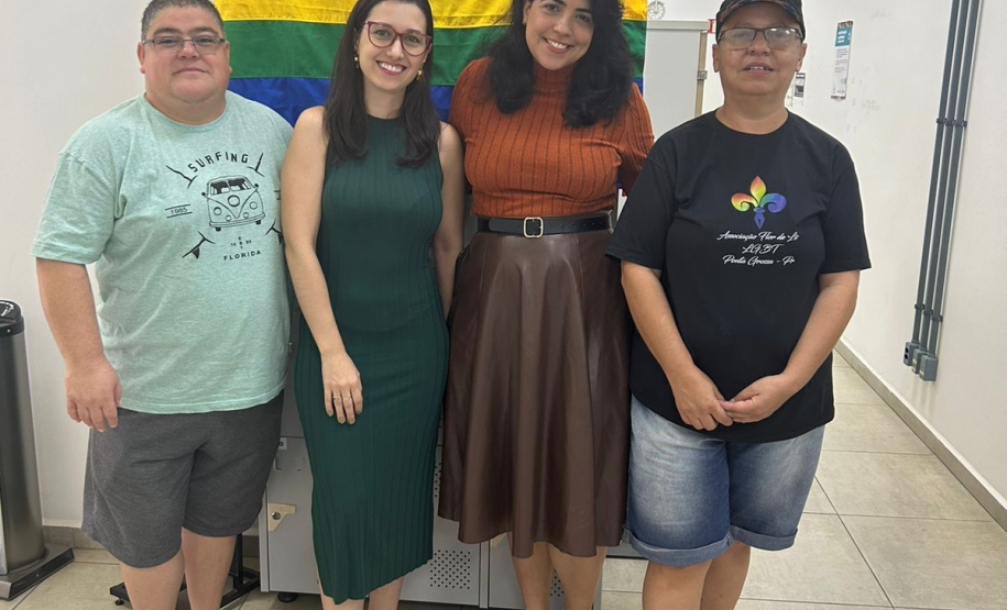 Imagem de uma foto espontânea de servidoras públicas e usuários, no fundo da imagem, dá para ver uma bandeira LGBTQIA+.