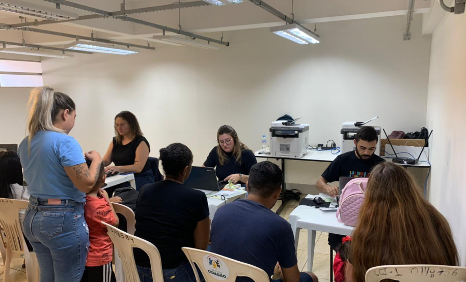 Imagem com a foto de usuários e usuárias da Defensoria recebendo o atendimento sentamos em cadeiras e mesas brancas dentro de uma sala.