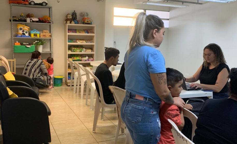 Imagem com a foto de usuários e usuárias da Defensoria recebendo o atendimento sentamos em cadeiras e mesas brancas dentro de uma sala.