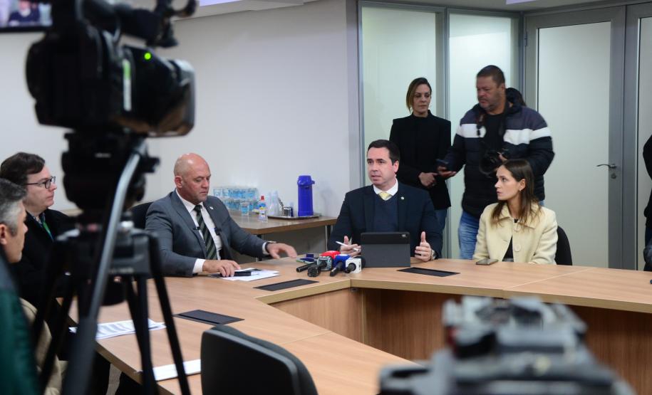Imagem com o diretor-geral da Polícia Científica, Luiz Rodrigo Grochocki, juntamento do secretário de Segurança Pública, Hudson Leôncio Teixeira, e do Defensor Público-Geral, Matheus Munhoz, sentados em uma mesa e se pronunciando durante a coletiva de imprensa