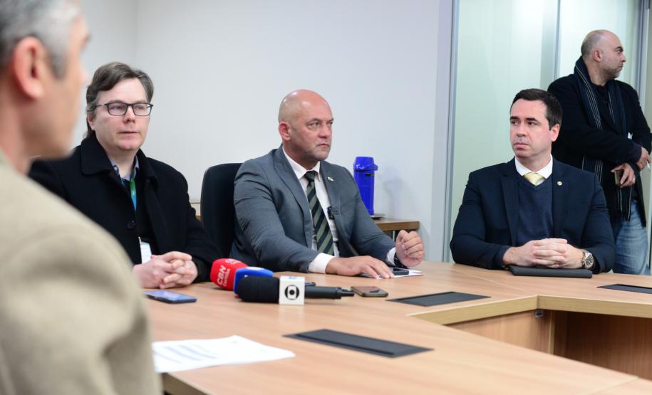 Imagem com o diretor-geral da Polícia Científica, Luiz Rodrigo Grochocki, juntamento do secretário de Segurança Pública, Hudson Leôncio Teixeira, e do Defensor Público-Geral, Matheus Munhoz, sentados em uma mesa e se pronunciando durante a coletiva de imprensa