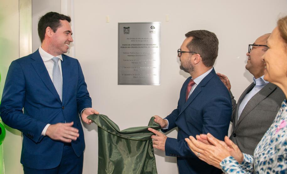 Imagem horizontal colorida em que se vê o descerramento da placa do novo Posto de Atendimento da DPE-PR na Câmara Municipal de Curitiba.