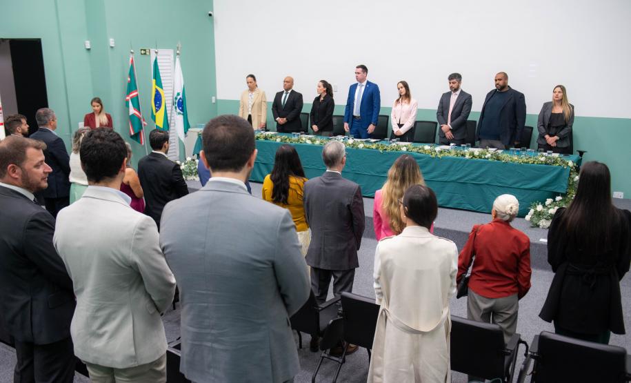 Imagem horizontal colorida onde se vê o público em primeiro plano e ao fundo a mesa de representantes da instituição que conduziram a cerimônia de posse dos novos Defensores Públicos do Paraná.