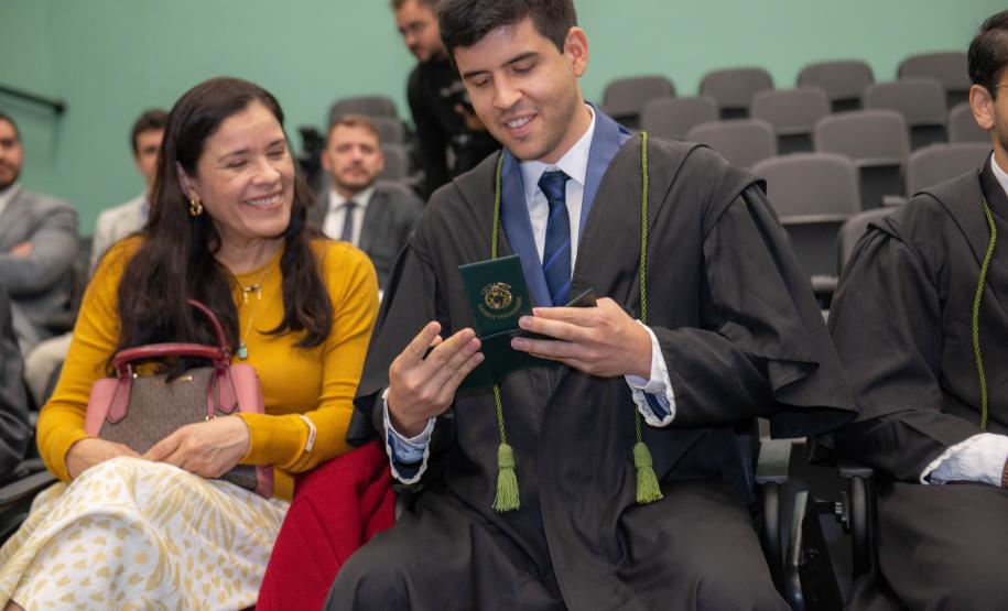 Imagem colorida horizontal onde novo Defensor Público empossado na cerimônia olha para carteira funcional.