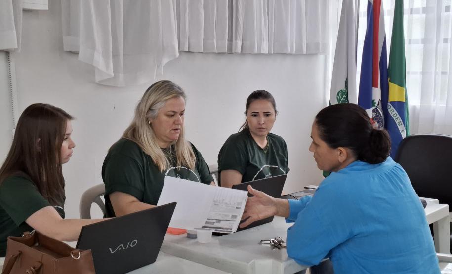 Imagem que mostra um dos atendimentos do evento. Três pessoas da Defensoria atendem uma mulher. Uma delas entrega um documento para a mulher que está sendo atendida.