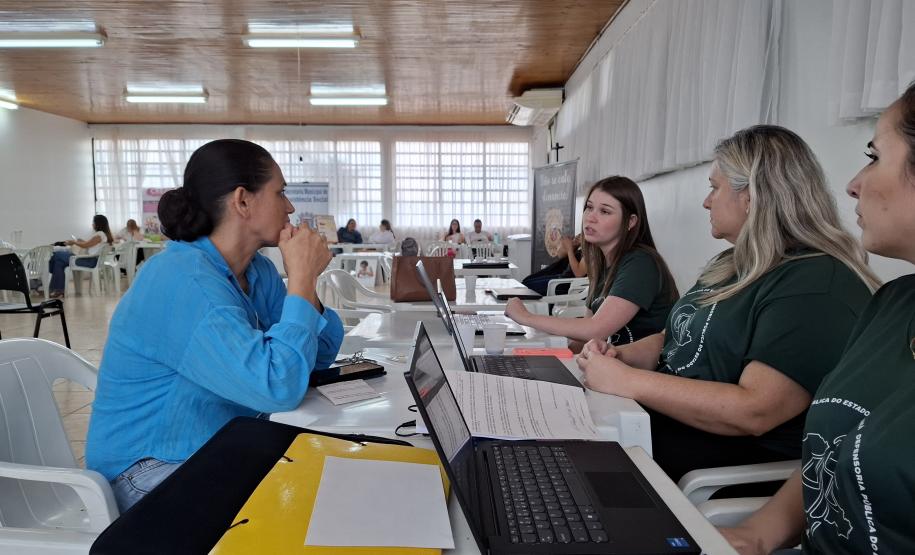 Imagem que mostra um dos atendimentos do evento. Três pessoas da Defensoria atendem uma mulher que escuta orientações delas.