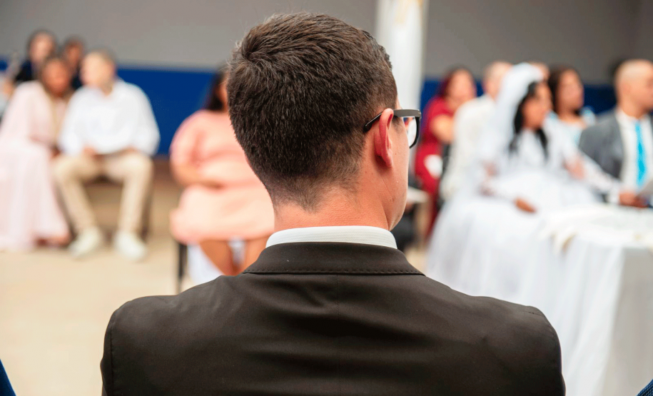 Imagem que mostra um homem sentado, de costas. Ao fundo é possível ver, de forma borrada, alguns casais sentados.