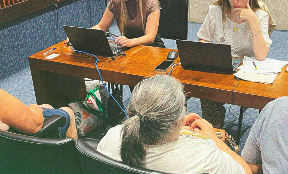 Imagem de uma foto de um atendimento presencial, duas servidoras públicas estão conferindo informações em seus notebooks enquanto três usuários da Defensoria Pública aguardam. Na parte central inferior da imagem, está o título da matéria.