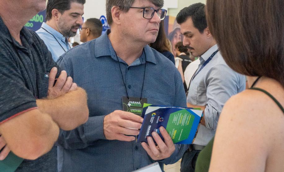 Imagem vertical colorida mostra o movimento de pessoas no estande da Defensoria Pública no evento Paraná Mais Cidades em Foz do Iguaçu.