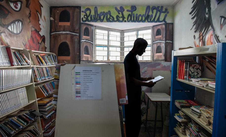 Imagem horizontal colorida em que se vê jovem na biblioteca da unidade socioeducacional.