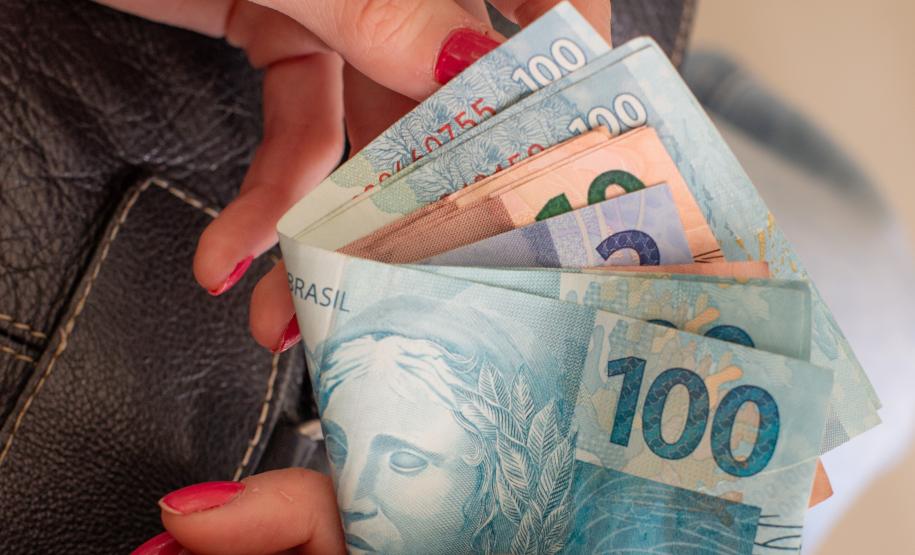 Imagem horizontal colorida em que aparecem as mãos de uma mulher com unhas feitas contando dinheiro.