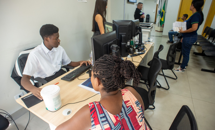 Atendimento ao público no interior da Defensoria, com servidores auxiliando cidadãos em balcões de recepção, em um ambiente iluminado e organizado.