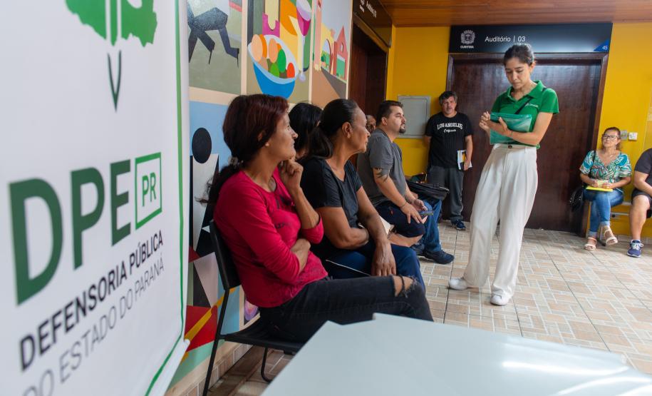 Imagem horizontal colorida em que se vê assistidos da Defensoria Pública recebendo as senhas para o mutirão de conciliação realizado em Santa Felicidade.