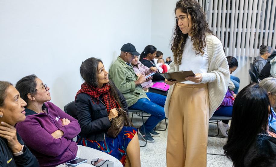 Imagem colorida horizontal em que se vê servidora da DPE-PR entregando as senhas e fazendo a orientação dos assistidos.