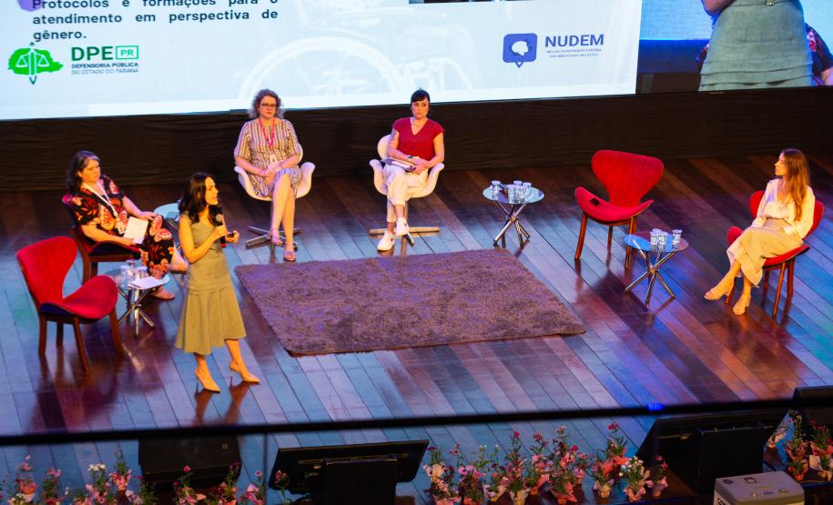Imagem horizontal colorida de um palco em que se vê a equipe da DPE-PR realiza uma oficina de capacitação sobre o Projeto Ampara