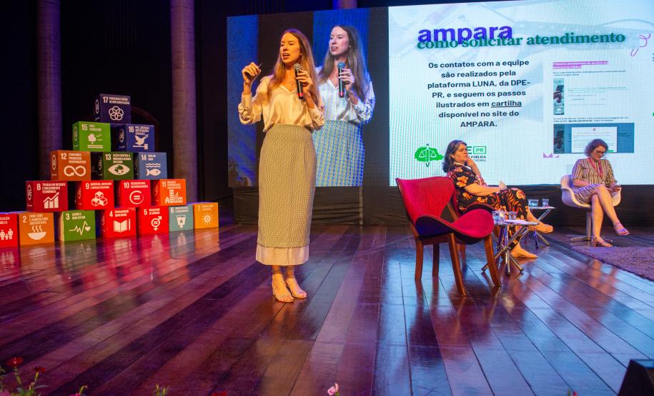 Imagem horizontal colorida de um palco em que se vê a equipe da DPE-PR realiza uma oficina de capacitação sobre o Projeto Ampara.