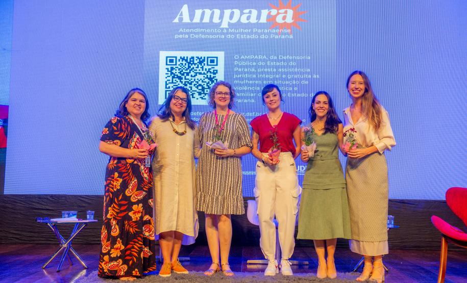 Imagem horizontal colorida de um palco onde a equipe da DPE-PR posa ao final da oficina de capacitação sobre o Projeto Ampara.