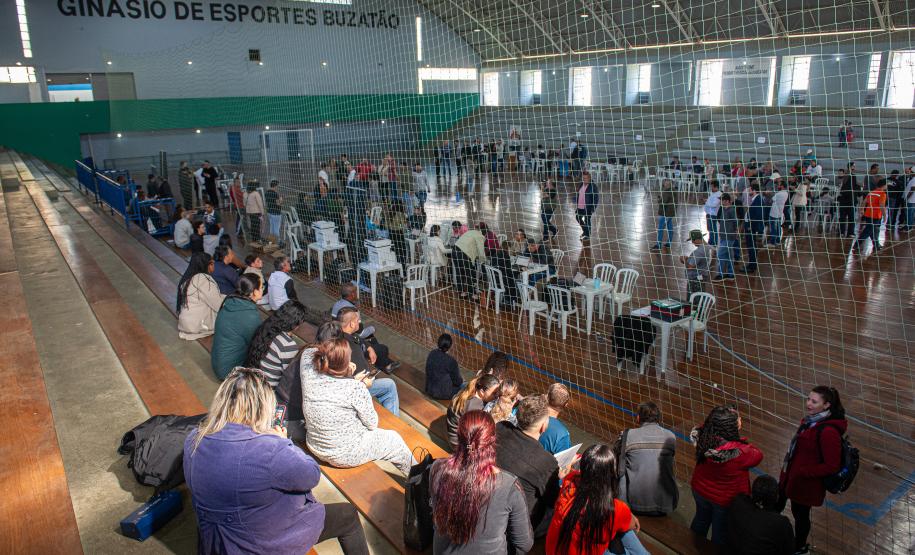 Imagem colorida horizontal mostra um plano geral do ginásio com pessoas aguardando os serviços do Mutirão e ao fundo as mesas onde são realizados os atendimentos.