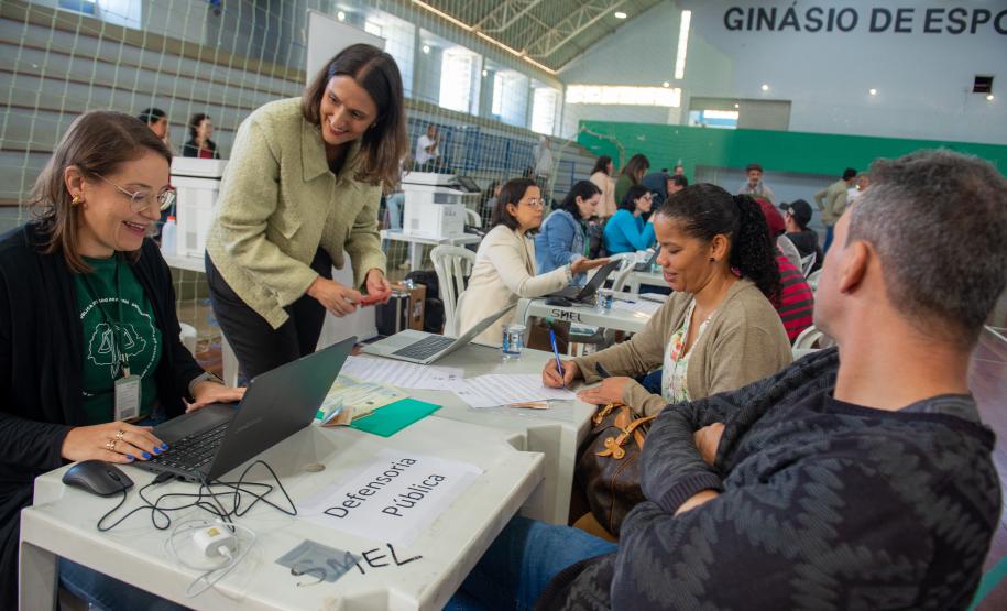 Imagem horizontal colorida em que se vê um casal de costas sentado enquanto a equipe da Defensoria Pública realiza atendimento jurídico em Mutirão realizado em Almirante Tamandaré.