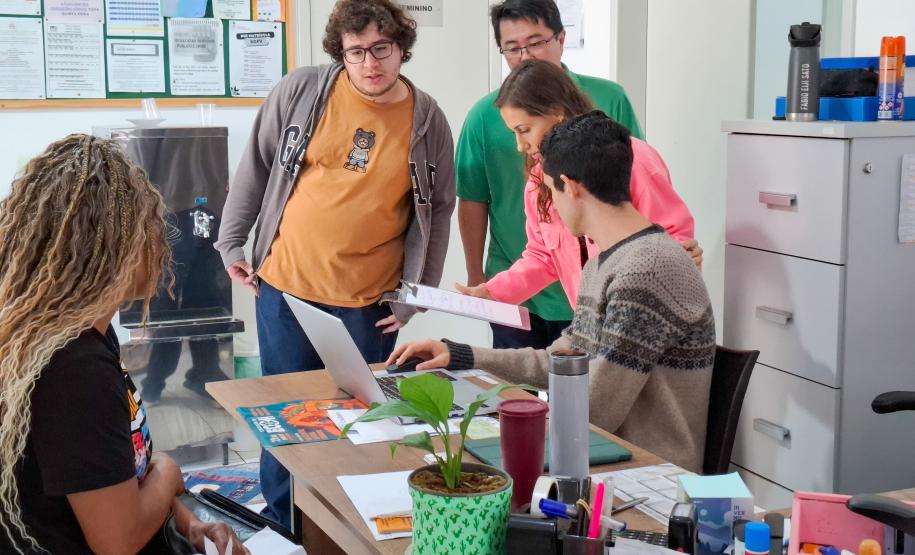 Assistida em primeiro plano de costas aguarda enquanto equipe da DPE-PR verifica seus documentos ao fundo.